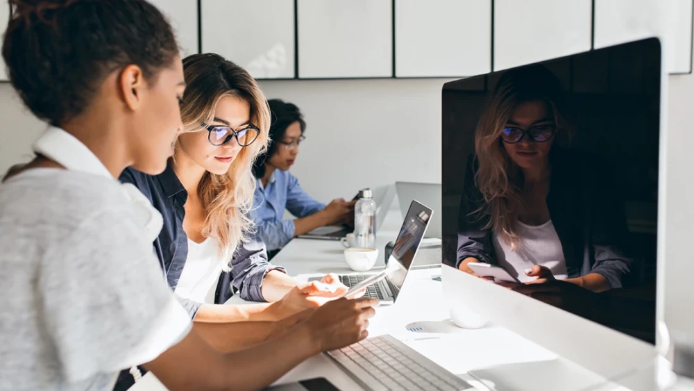 Group of people looking at a computer monitor and laptop.