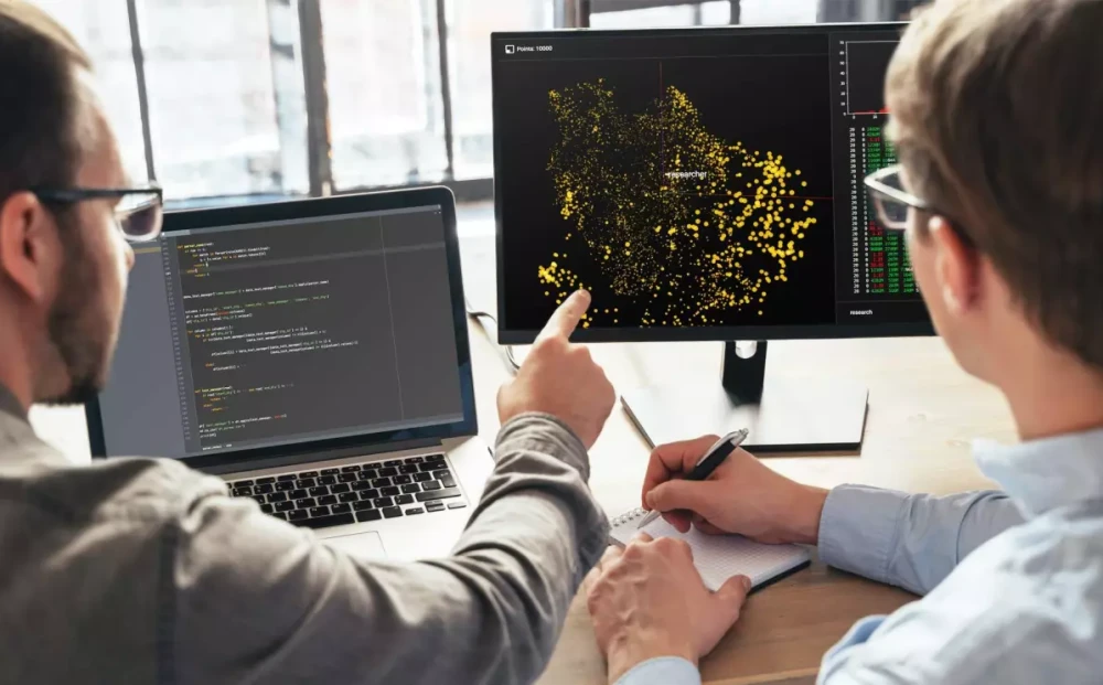Two people looking at map activity on a computer monitor.