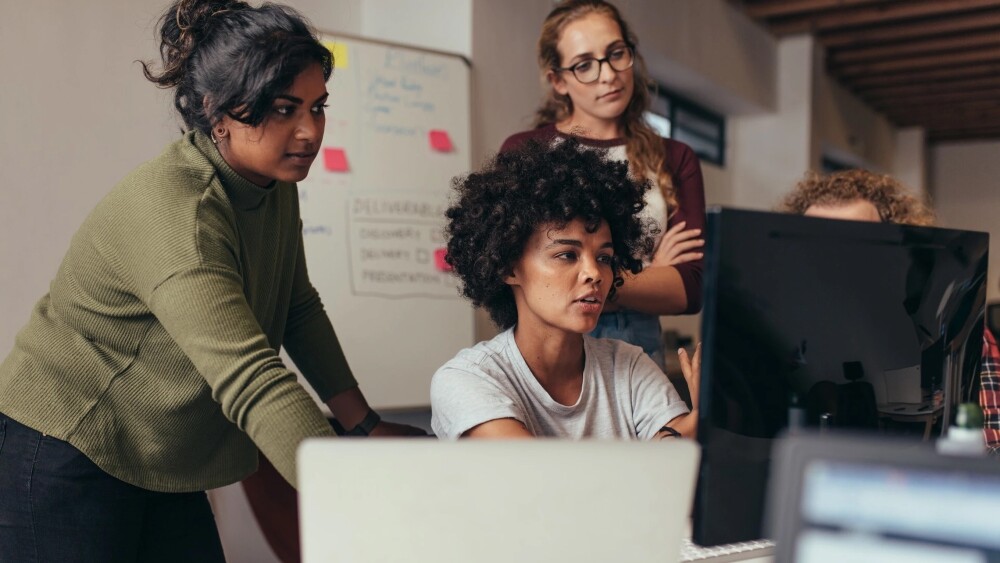 Group of professionals in an office setting collaborating together while looking at desktop computer monitor