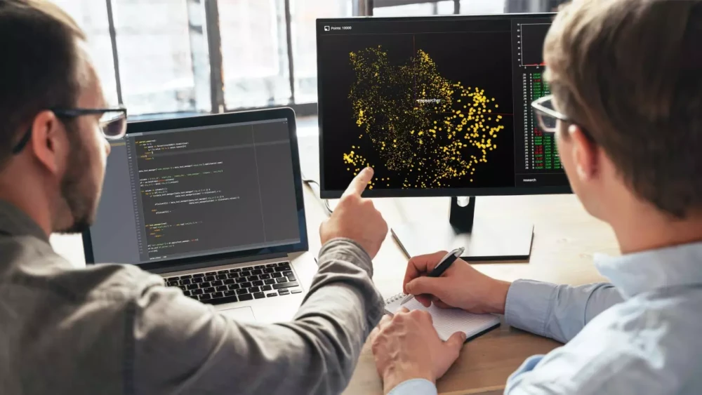 Two people looking at map activity on a computer monitor.