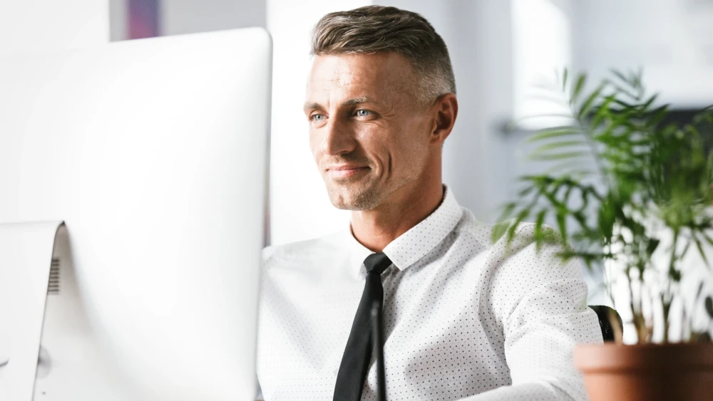 Smiling person wearing tie sitting at desktop computer